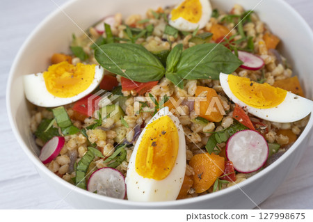 Healthy spelt salad with roasted vegetables, hard-boiled egg, and fresh herbs prepared in a rustic 127998675