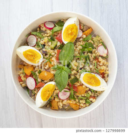 Healthy spelt salad with roasted vegetables, hard-boiled egg, and fresh herbs prepared in a rustic 127998699