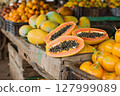 Fresh tropical fruits including papaya and mango displayed on rustic wooden market stand. 127999089