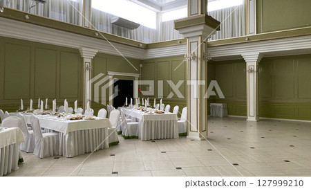 Spacious banquet hall with high ceilings, decorative columns, and elegant white-covered tables set for formal dining. Ideal venue for weddings, receptions, and upscale events 127999210