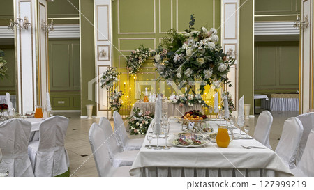 Elegant banquet hall with a beautifully decorated table featuring floral arrangements, crystal glasses, and a serene atmosphere. Perfect setting for a wedding, celebration, or special event Elegant banquet hall with a beautifully decorated table featuring floral arrangements, crystal glasses, and a serene atmosphere. Perfect setting for a wedding, celebration, or special event 127999219