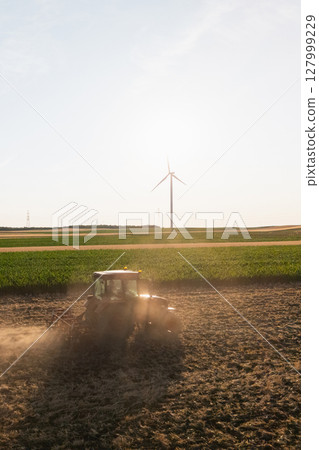 Agricultural tractor is working on the field with wind turbines. Aerial view. Agricultural tractor is working on the field with wind turbines. Aerial view. 127999229