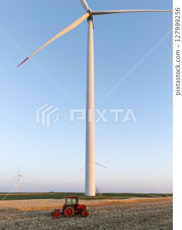 Agricultural tractor is working on the field with wind turbines. Aerial view. 127999256