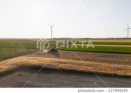 Agricultural tractor is working on the field with wind turbines. Aerial view. 127999265