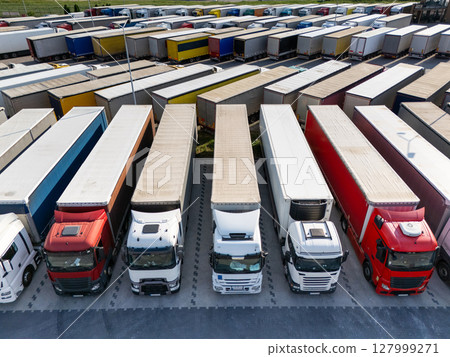 Aerial view of a large truck parking lot at a logistics hub, with multiple commercial semi trucks parked in organized rows. 127999271