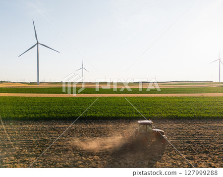 Agricultural tractor is working on the field with wind turbines. Aerial view. Agricultural tractor is working on the field with wind turbines. Aerial view. 127999288