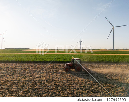 Agricultural tractor is working on the field with wind turbines. Aerial view. Agricultural tractor is working on the field with wind turbines. Aerial view. 127999293