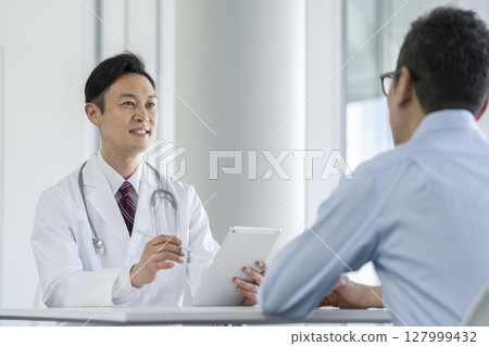 A male doctor holding a tablet and asking questions A male doctor holding a tablet and asking questions 127999432
