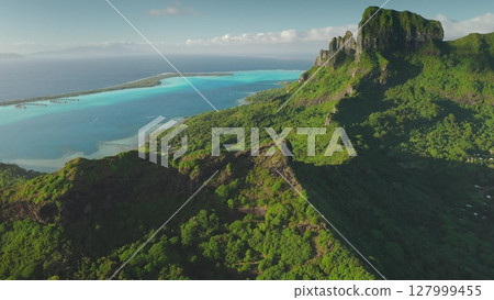 Aerial drone of stunning beauty Bora Bora tropical island, green forest vegetation, turquoise lagoon, and majestic mount Otemanu under a clear blue sky. Wild travel destination, remote nature Aerial drone of stunning beauty Bora Bora tropical island, green forest vegetation, turquoise lagoon, and majestic mount Otemanu under a clear blue sky. Wild travel destination, remote nature 127999455