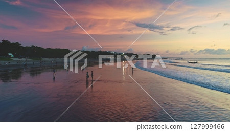 Dreamland Beach in Bali, Indonesia, offers a breathtaking view during sunset, with tourists enjoying the colorful sky and calm ocean waves, creating a serene and picturesque scene 127999466
