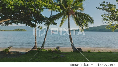 Sailboats gliding across Savusavu Bay, surrounded by swaying palm trees and vibrant vegetation, create a picturesque scene on a sunny summer day in Vanua Levu, Fiji. Amazing nature travel background 127999468