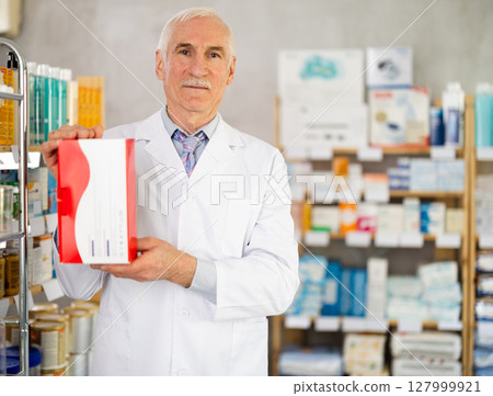 Elderly male pharmacist offers box with medical device Elderly male pharmacist offers box with medical device 127999921