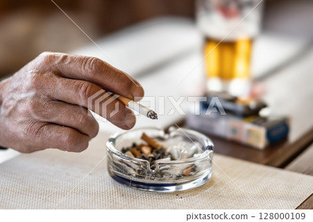 The hand of a smoking man or woman on a table led an ashtray with draft beer in a pub 128000109