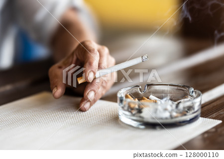 The hand of a smoking woman with a cigarette taps the ash into an ashtray The hand of a smoking woman with a cigarette taps the ash into an ashtray 128000110
