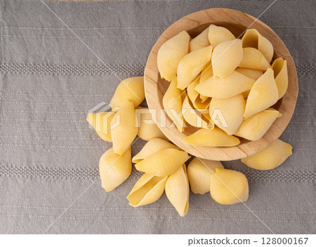 Raw conchiglioni pasta in wood bowl. Dry conchiglie noodle in shell shape 128000167