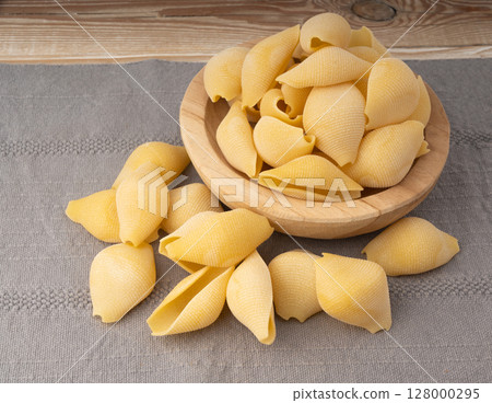 Raw conchiglioni pasta in wood bowl. Dry conchiglie noodle in shell shape 128000295