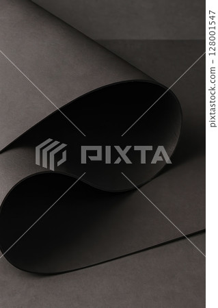Minimal closeup of rolled black vegan leather sheet with smooth matte surface, elegant curves  Minimal closeup of rolled black vegan leather sheet with smooth matte surface, elegant curves  128001547