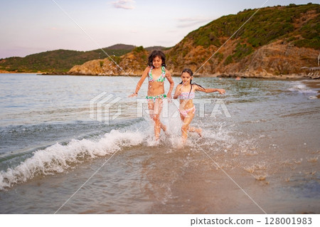 Joyful sisters splashing in the waves at a beautiful sunset beach Joyful sisters splashing in the waves at a beautiful sunset beach 128001983
