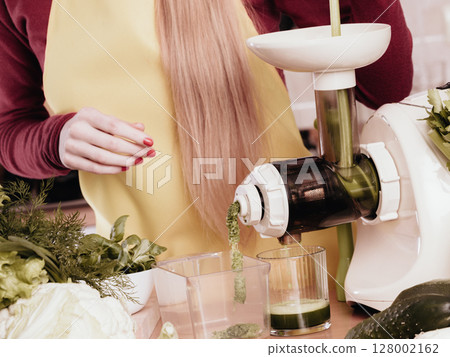 Woman in kitchen making vegetable smoothie juice Woman in kitchen making vegetable smoothie juice 128002162