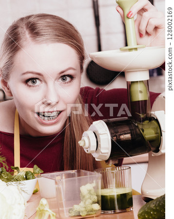 Woman in kitchen making vegetable smoothie juice 128002169