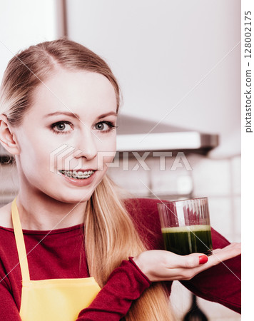 Woman in kitchen holding vegetable smoothie juice Woman in kitchen holding vegetable smoothie juice 128002175
