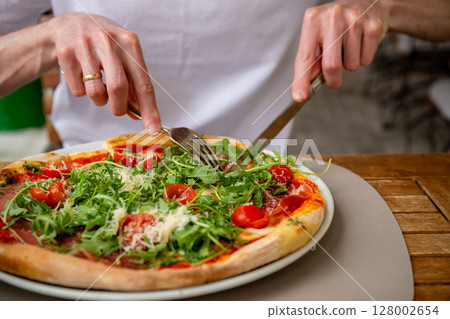 Fresh Italian pizza with arugula, cherry tomatoes, prosciutto and parmesan served at outdoor cafe 128002654