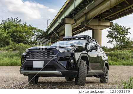 A black car parked on the riverbank, blue sky and a bridge A black car parked on the riverbank, blue sky and a bridge 128003179