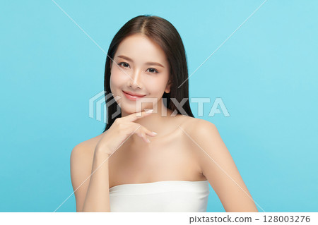 A beautiful young Asian woman with clean, fresh skin against a blue background. Skincare, facial treatment, cosmetology, beauty, and spa. An elegant portrait of an Asian woman. 128003276