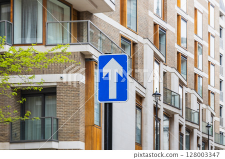 Blue one way traffic sign with upward arrow on modern city street near contemporary flats 128003347