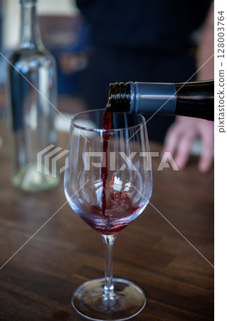 A man is pouring red wine in the glass A man is pouring red wine in the glass 128003764