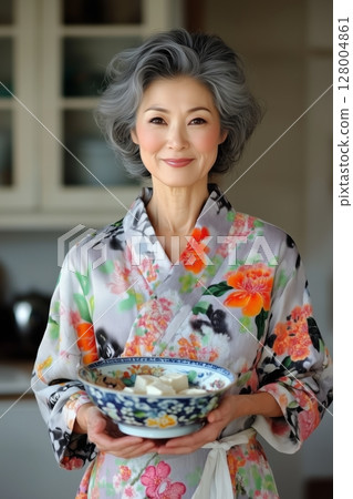 Asian woman stands gracefully, offering freshly prepared meal in artistic dishware. Muted tones complement delicate beauty. Asian woman conveys warmth, tradition, and care. 128004861