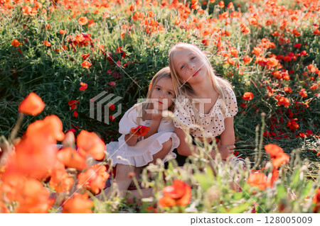 Sisters on plaid in a blooming poppy field, sunny summer day 128005009