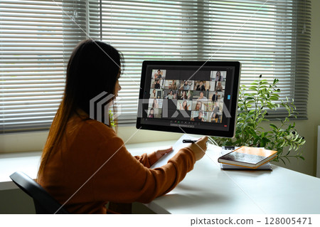 Young woman attending an online video conference call with multiple colleagues displayed on computer screen Young woman attending an online video conference call with multiple colleagues displayed on computer screen 128005471