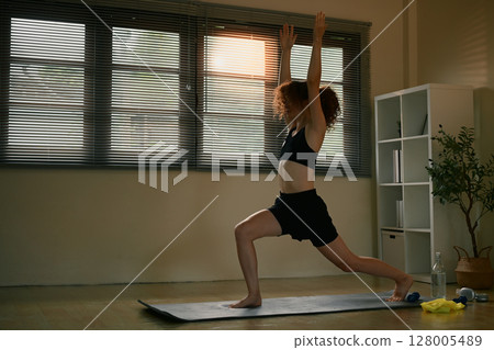 Young woman practicing yoga in a bright home studio, to improve strength and balance 128005489