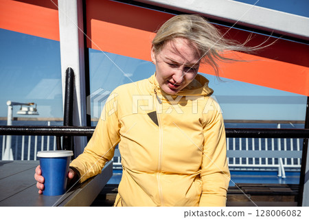 Woman in yellow jacket holding coffee cup on windy ferry deck in bright sunlight Woman in yellow jacket holding coffee cup on windy ferry deck in bright sunlight 128006082