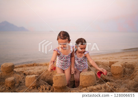 Joyful children building sandcastles at the sunset beach Joyful children building sandcastles at the sunset beach 128006655