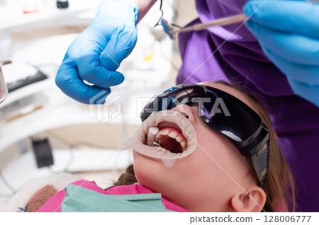 Child receiving dental care in a bright clinic, surrounded by professional staff and modern technology during a routine check-up Child receiving dental care in a bright clinic, surrounded by professional staff and modern technology during a routine check-up 128006777