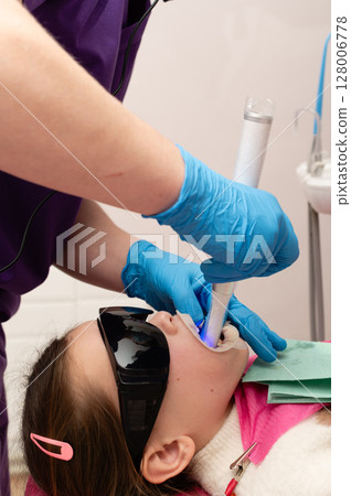 Child undergoing dental treatment with specialized tools and protective eyewear in a modern clinic during a bright weekday afternoon Child undergoing dental treatment with specialized tools and protective eyewear in a modern clinic during a bright weekday afternoon 128006778