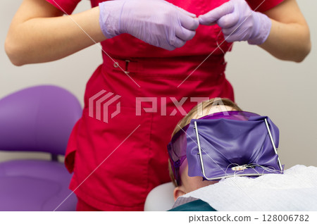 Patient in dental chair undergoing procedure while hygienist prepares instruments in a clinical setting, captured in a modern dental office environment 128006782