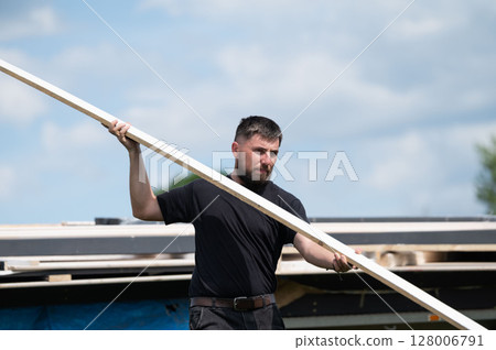 A man carries a wooden board to install a wooden gazebo in a lavender field. 128006791