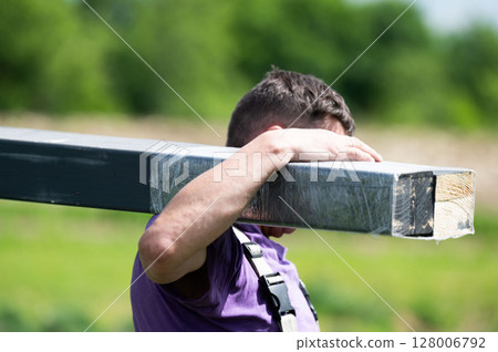 A man carries a wooden beam for installing a gazebo in a lavender field. 128006792