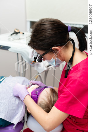 Caring dentist conducts a pediatric dental procedure while ensuring comfort and safety in a bright, modern clinic during the afternoon Caring dentist conducts a pediatric dental procedure while ensuring comfort and safety in a bright, modern clinic during the afternoon 128006907