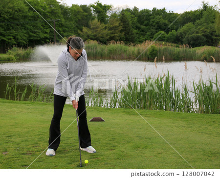 Golf Practice Session by the Serene Pond in a Lush Park Setting 128007042