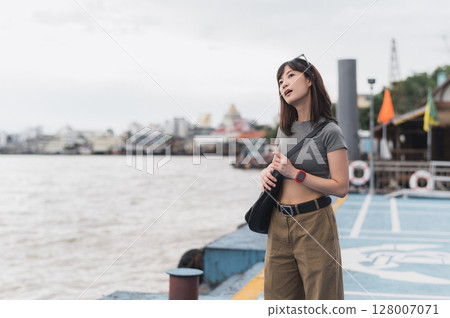 Contemplative solo southeast asian woman teenager blogger and world travel explorer wait for express boat. Local cultural experience asia tourism concept by Chao Phraya river Bangkok Thailand 128007071