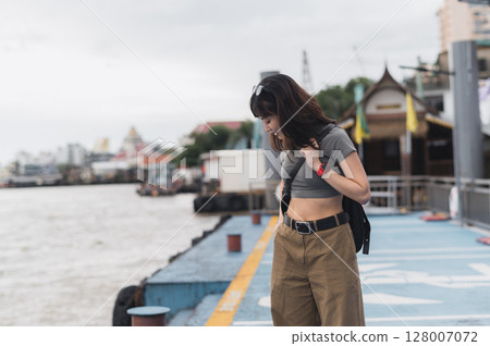 Solo southeast asian woman teenager blogger smartphone wait express boat friend Chao Phraya river Bangkok. World travel explorer tourism concept local cultural experience Thailand Asia Solo southeast asian woman teenager blogger smartphone wait express boat friend Chao Phraya river Bangkok. World travel explorer tourism concept local cultural experience Thailand Asia 128007072