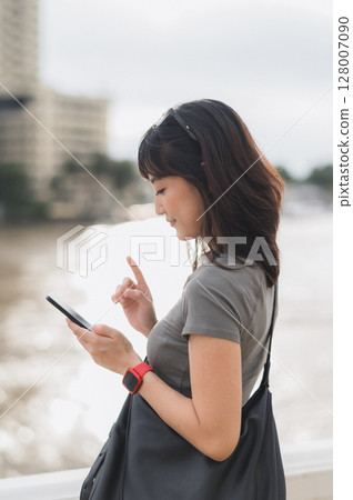 Young southeast asian woman teenager blogger explorer searching map smartphone for world travel guide. Tourism concept for local cultural experience asia by Chao Phraya River Bangkok Thailand Young southeast asian woman teenager blogger explorer searching map smartphone for world travel guide. Tourism concept for local cultural experience asia by Chao Phraya River Bangkok Thailand 128007090
