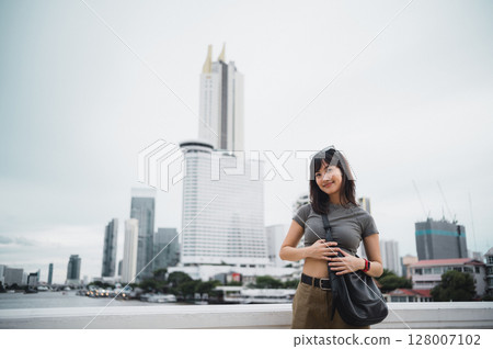 Happy solo young southeast asian woman teenager blogger explorer enjoying world travel. Local cultural tourism experience concept with smartphone in Bangkok Thailand Asia by Chao Phraya River 128007102