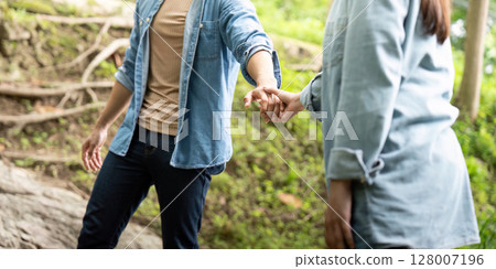 Couple holding hands in nature. Young man and woman sharing a moment of connection by a stream. Couple holding hands in nature. Young man and woman sharing a moment of connection by a stream. 128007196