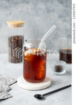 Cold brew coffee in a glass with ice on a marble stand on a light concrete background 128007935