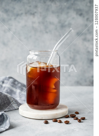 Cold brew coffee in a glass with ice on a marble stand on a light concrete background  128007937